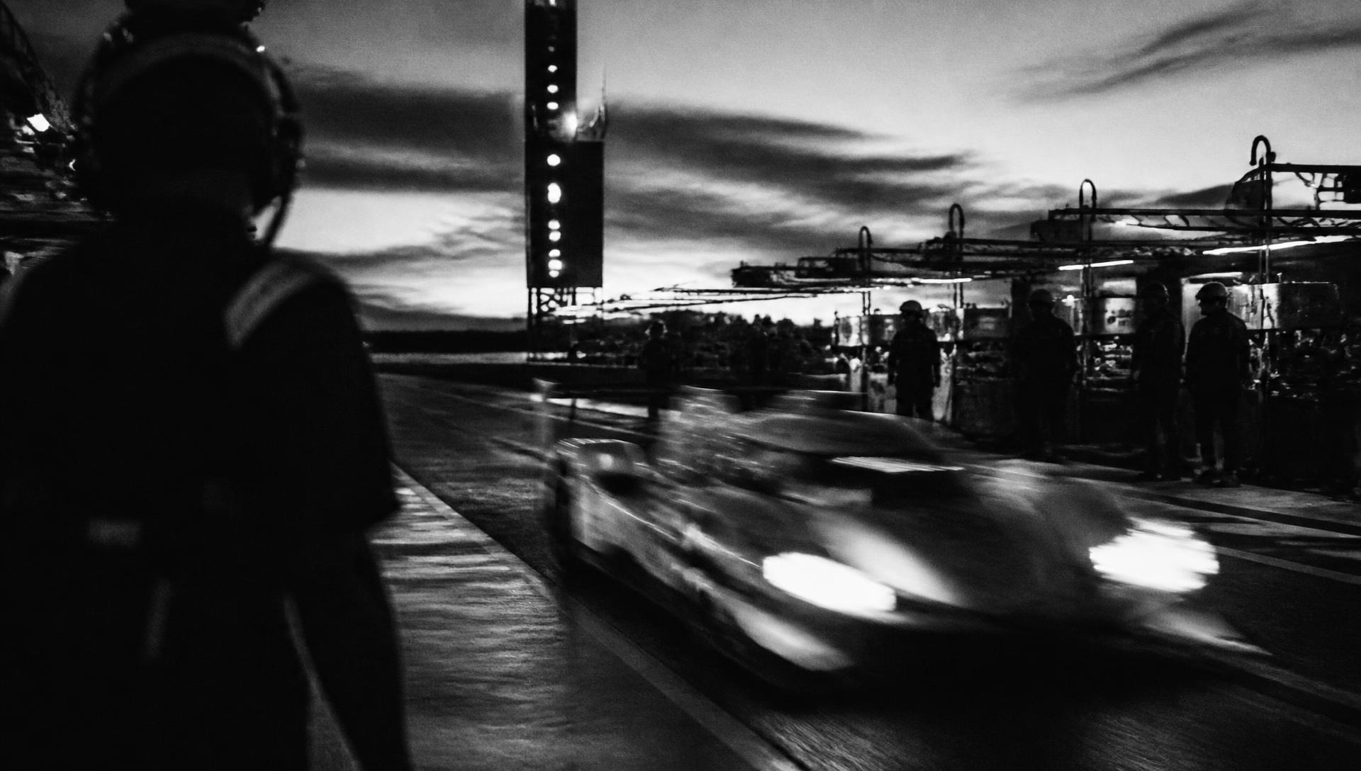 Endurance race car passing a pit lane at dusk, monochrome film still